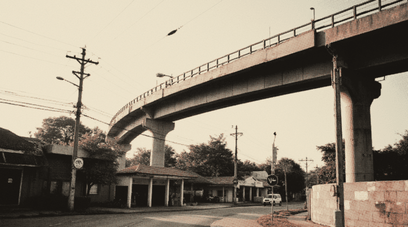 An elevated rail viaduct curving on tall concrete piers over an empty road at dawn — LRT3 Shah Alam Line 2026: Station List and Fares
