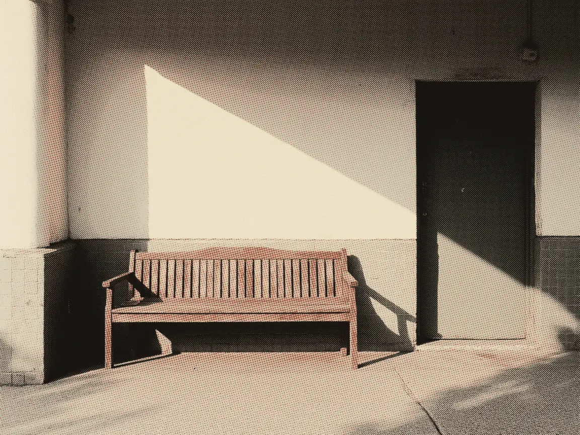 An empty wooden bench in a wedge of morning light beside a closed door