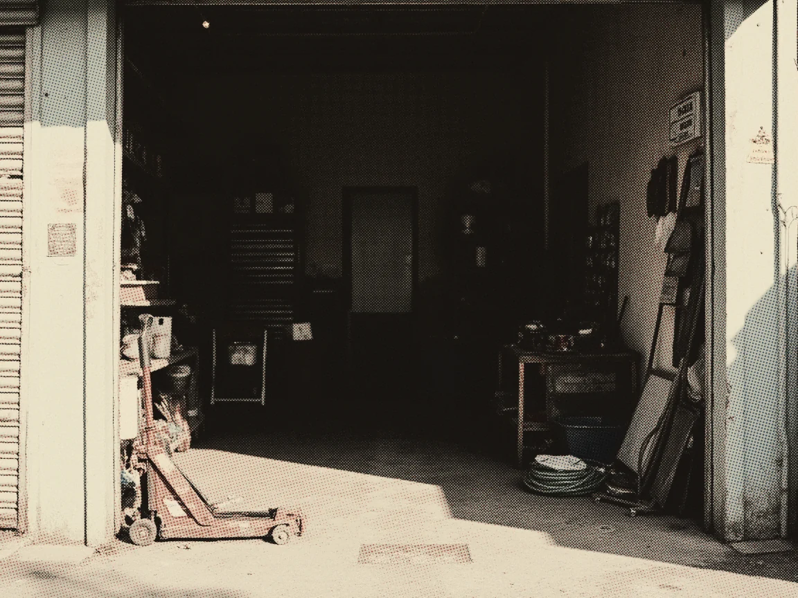 Car Battery Price Malaysia 2026: Century vs Amaron — a roadside workshop with its shutter half up, a trolley jack and an air hose on the floor