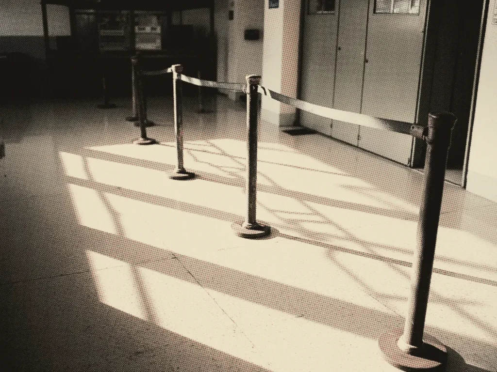 A row of queue-barrier posts with retractable belts forming a line across a sunlit hallway